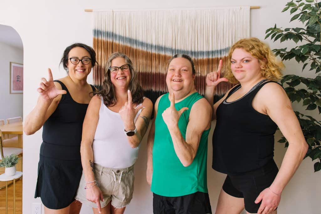 A group of four female lipodystrophy patients hold their fingers up in the shape of an L for World Lipodystrophy Day